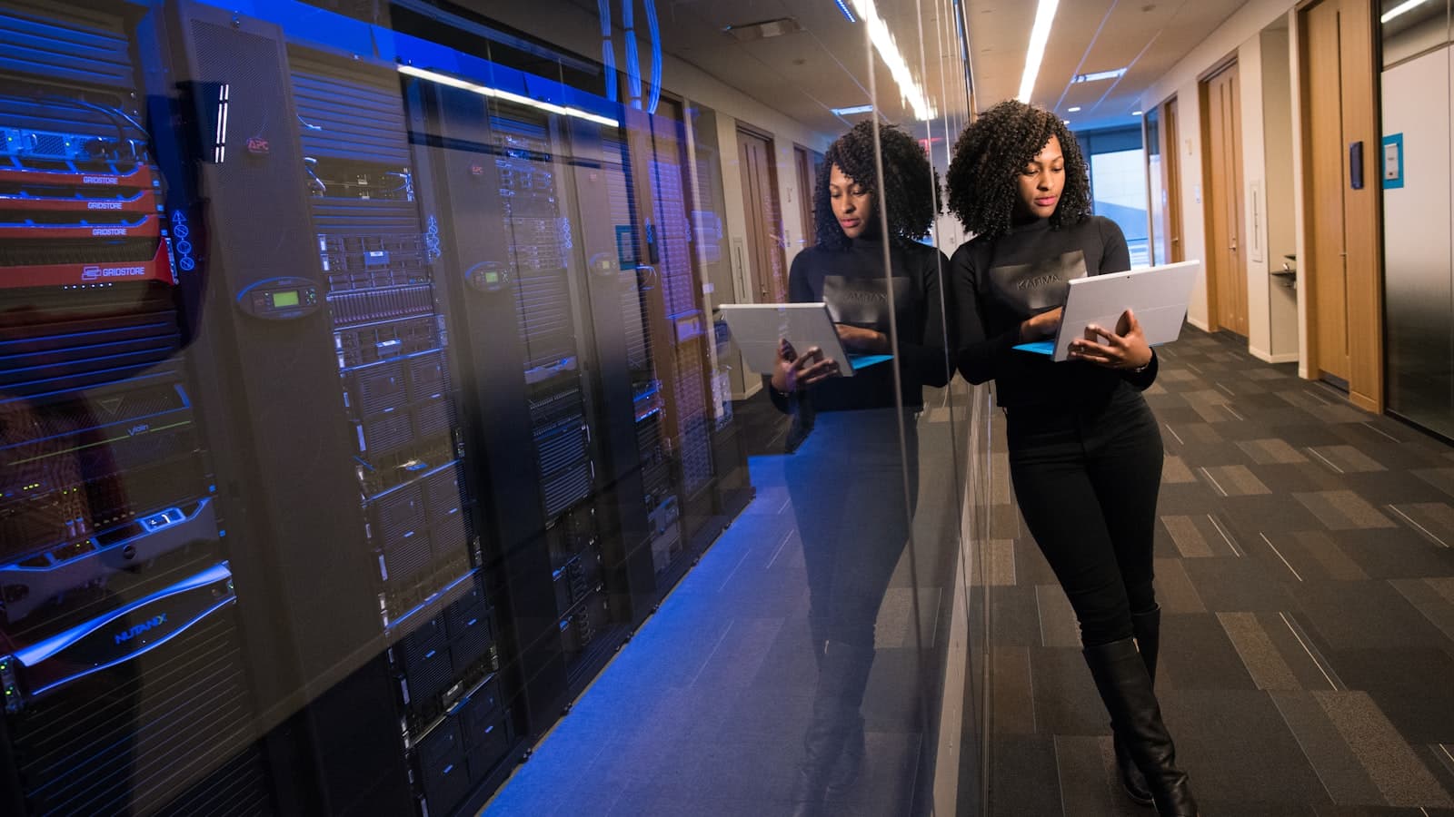 Two people walking with tablets through a dimly lit data center corridor lined with server racks
