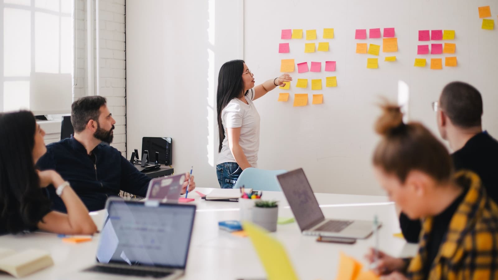 Person presenting ideas from a wall of colored sticky notes to a seated team